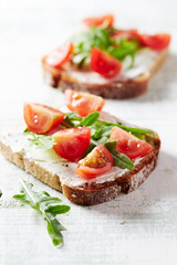 Tasty sandwiches with cream cheese, cherry tomatoes and fresh herbs. Bright wooden background. Close up. 