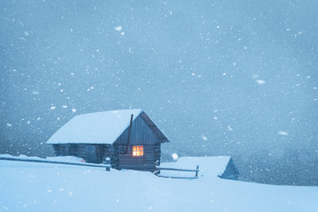 Fototapeta na wymiar Fantastic winter landscape with wooden house in snowstorm in snowy mountains. Christmas holiday and winter vacations concept