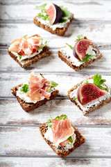Tasty sandwiches with cream cheese, smoked ham and figs. Bright wooden background. 