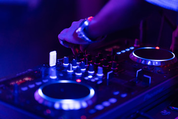 Obraz na płótnie Canvas club dj plays music on stage in nightclub.Hand of disc jockey adjusting sound track volume level.Professional audio equipment on music festival