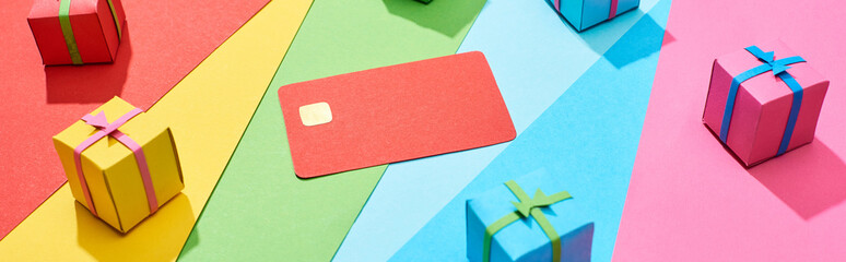 red empty credit card and multicolored gift boxes on rainbow background, panoramic shot
