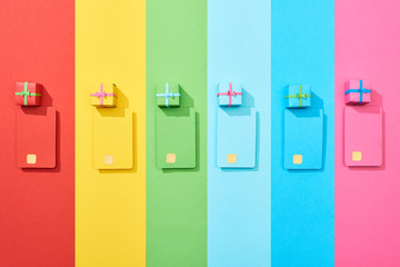 top view of multicolored empty credit cards and gift boxes on rainbow background