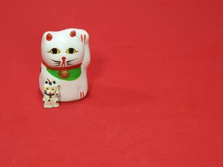 Two little Maneki Neko, Japanese lucky cats, amulets that bring good luck, protection, prosperity, health and happiness. They look like father (mother) and son. Red background.