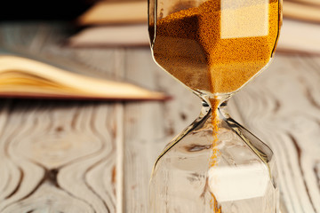 Sandglass on wooden table with opened book close up