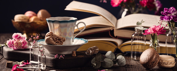 Cup of coffee, old books and pink carnation flowers on old wooden background. Mothers day, birthday greeting card. Copy space, banner.