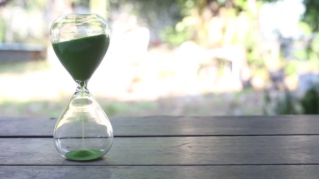Green sand running through bulbs of  hourglass on wooden table, As passing time
