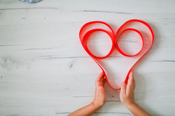 Red heart love symbol from red ribbon on wooden background.