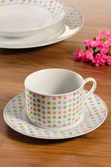 Coffee cup set with saucer on a wooden table with set of dishes in the background
