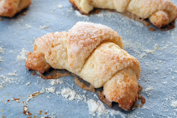 Baked bagels from a curd dough with sugar lying on a parchment paper covered with flour. Sweet ruddy croissants just taken out of the oven. A delicious tea snack for breakfast