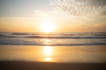 Wide panorama of waves coming in at the Arpoador Devil's beach in Rio de Janeiro, Brazil, at sunrise with the sun reflecting in the water that hits the pristine sand beach