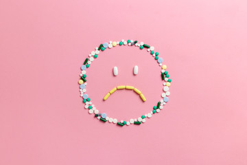 Composition of pills and capsules on a pink background in the form of emoji. Sad emotions....