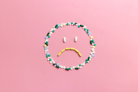 Composition of pills and capsules on a pink background in the form of emoji. Sad emotions. Psychological help. Copy space. View from above. Flat lay.