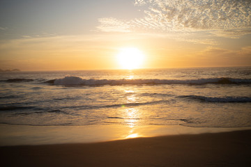 Deep orange colours with waves coming in at the Arpoador Devil's beach in Rio de Janeiro, Brazil, at sunrise with the sun reflecting in the water that hits the pristine sand beach