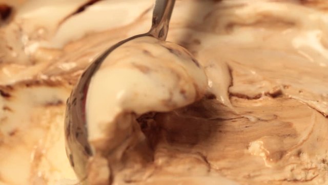 Close up caramel and chocolate ice cream scooping out of container with metal spoon