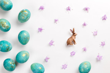 Happy easter card. Stylish minimalistic composition of turquoise with gold easter eggs on a white background. Figurine of a rabbit and delicate spring flowers. Flat lay, top view, copy space