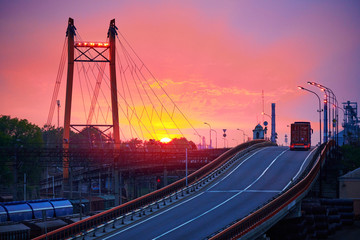 truck with container rides over the bridge, beautiful sunset, freight cars in industrial seaport, the road goes up