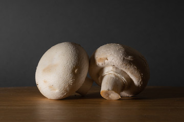 White champignon mushrooms lie on a wooden table on a dark background. Side view.