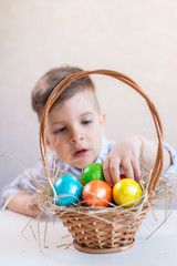 Little boy takes an Easter egg from the basket from the table on a white background.