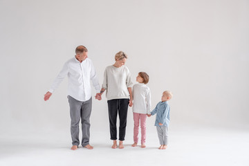 Naklejka premium Positive loving family dad pregnant mom sister and brother holding hands looking at each other posing barefoot in the studio on a white background. Happy family relationship concept. Copyspace