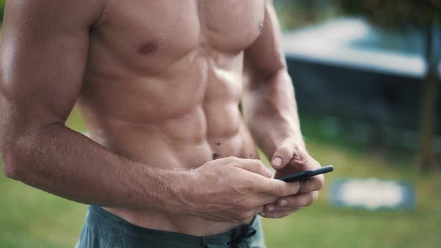 Close up, shirtless man with muscular body uses mobile phone and sends message