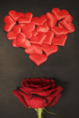 Red rose bud below a heart made of smaller cloth hearts, against dark black background. Valentines...