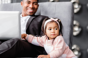 Little cute daughter distracts father from serious work. Parenting and business. African girl asks...