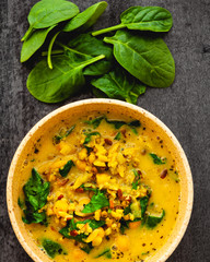 Flat lay of yellow soup in a bowl plate. Some spinach leaves (soup ingredient) above the bowl.