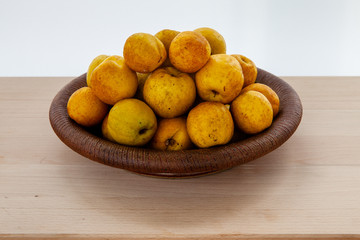 Bowl full of small and round Japanese quinces. Grey background.