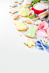 Sweet Easter baking cooking background with traditional Easter bunny and egg cookies, sugar sprinkles, ingredients, utensils. White table background copy space layout