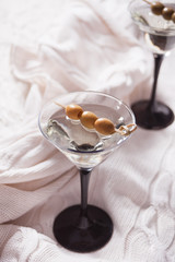 Two glasses of martini with olives on the white knitted plaid