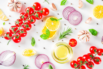 Cooking background with spices, vegetables and herbs fresh basil, rosemary, tomato, garlic, onions, lemon on a white kitchen table. Layout top view copy space. Healthy ingredients for cooking