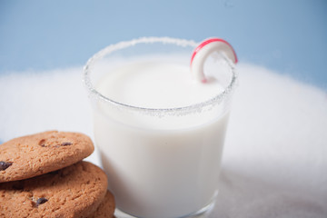 Glass of milk, candy cane, homemade cookies and snow on the blue background