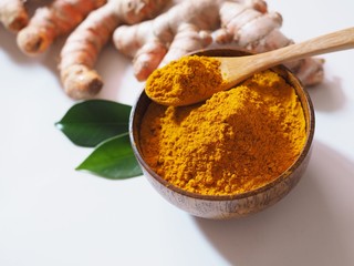 Turmeric root and turmeric powder in wooden bowl with leaf