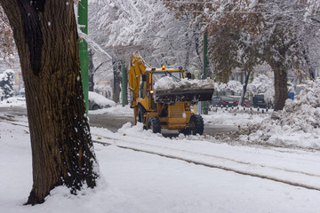 Yellow tractor with snowplow removing snow from the streets. 