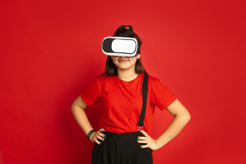 Asian teenager's portrait isolated on red studio background. Beautiful female brunette model with long hair in casual style. Concept of human emotions, facial expression, sales, ad. Plays VR-headset.