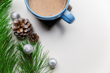 Obraz na płótnie Canvas Blue cup of hot cacao or cappuccino with cinnamon standing on white table with pine branches and silver bulbs. Merry Christmas, Happy New Year and winter holidays concept. Copy space.