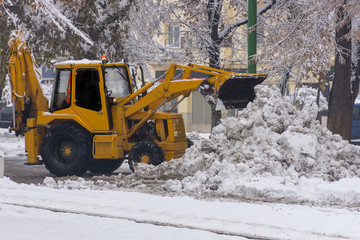 Yellow tractor with snowplow removing snow from the streets. 