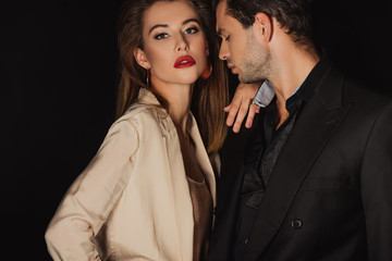 attractive woman hugging handsome man in suit isolated on black