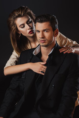 attractive woman hugging handsome man in suit isolated on black