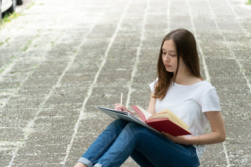 Fototapeta premium Teenage girl studying sitting on the walkway, outdoors