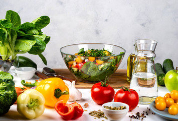 Bowl full of salad from different eco vegetables with ingredients and spices on the table. Healthy diet food concept.