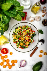 Homemade salad from various organic vegetables in a glass bowl with ingredients and spices on white background. Top view. Healthy diet food concept