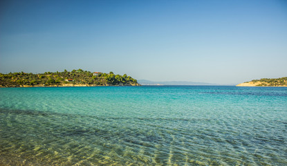 Fototapeta premium Greece beach cozy Aegean sea lagoon transparent aquamarine shallow water with horizon background view islands coast line in summer tine clear weather