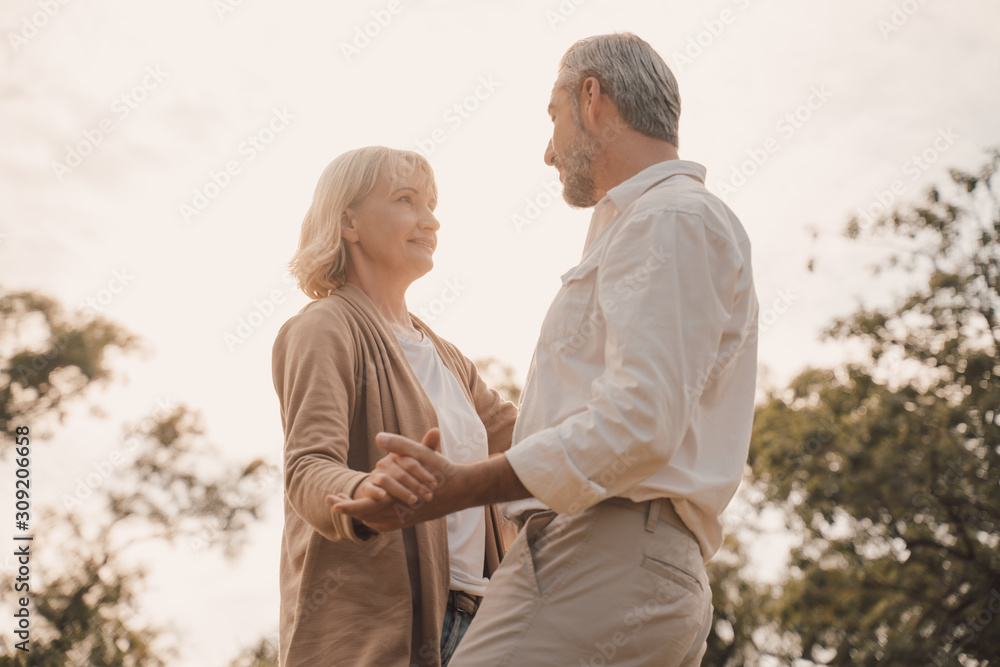 Wall mural Romantic and elderly healthy lifestyle concept.Senior active caucasian couple holding hands looks happy in the park in the afternoon autumn sunlight,happy anniversary,happily retired with copy space.