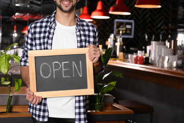 Young business owner holding sign OPEN in his cafe, closeup. Space for text