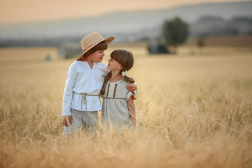 Two children a boy and a girl of preschool age walk together in a wheat field.