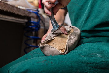 Obraz premium close up of orthopedic shoemaker covering a wooden last with leather 