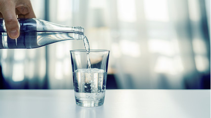 Nalewanie oczyszczonej świeżej wody do picia z butelki na stole w salonie - obrazy, fototapety, plakaty