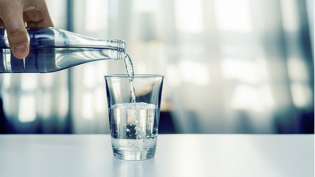 Nalewanie oczyszczonej świeżej wody do picia z butelki na stole w salonie