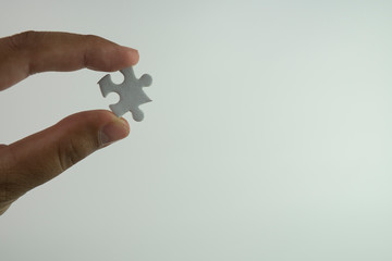 Hand holding white jig saw piece isolated white background.